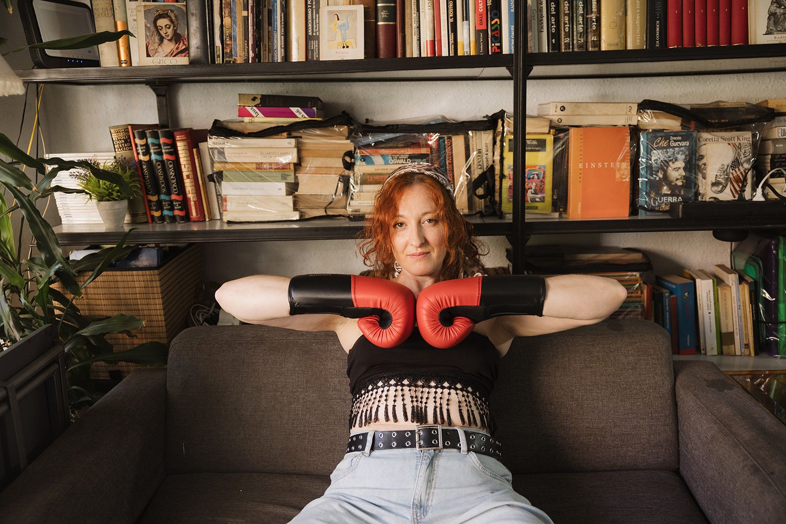 Nunu (Núria Santosjuanes) con guantes de boxeo, sentada frente a una estantería de libros