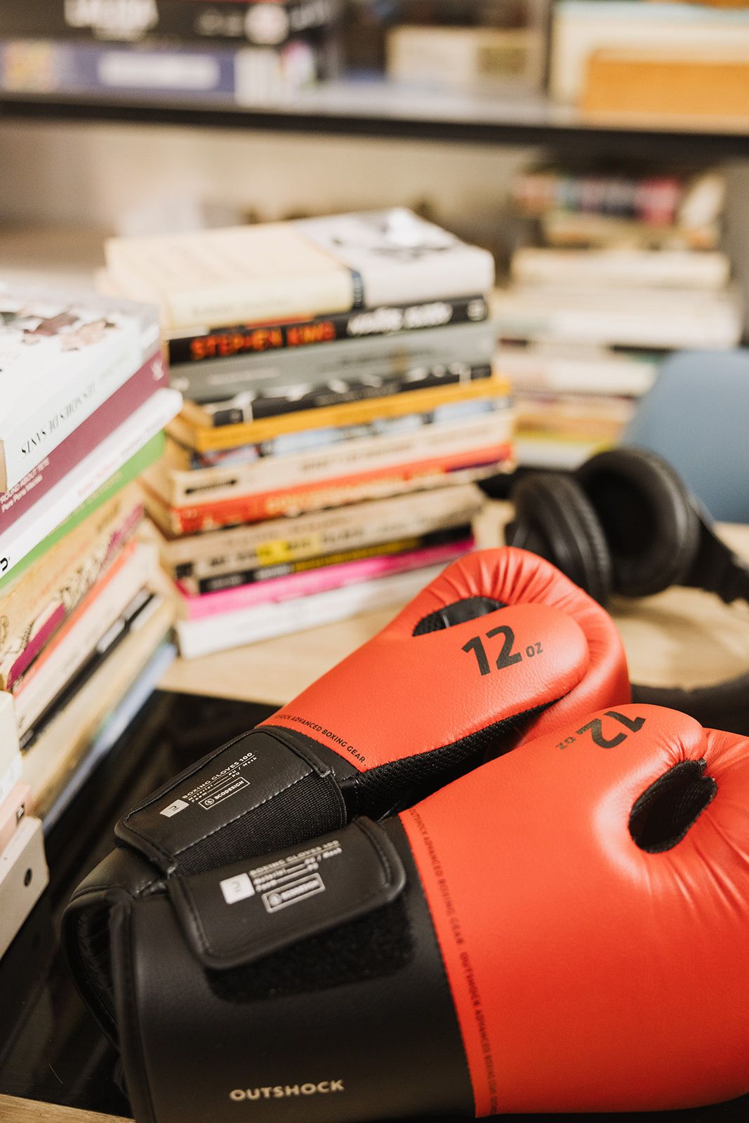 Guantes de boxeo de 12 onzas junto a una pila de libros y unos auriculares de estudio