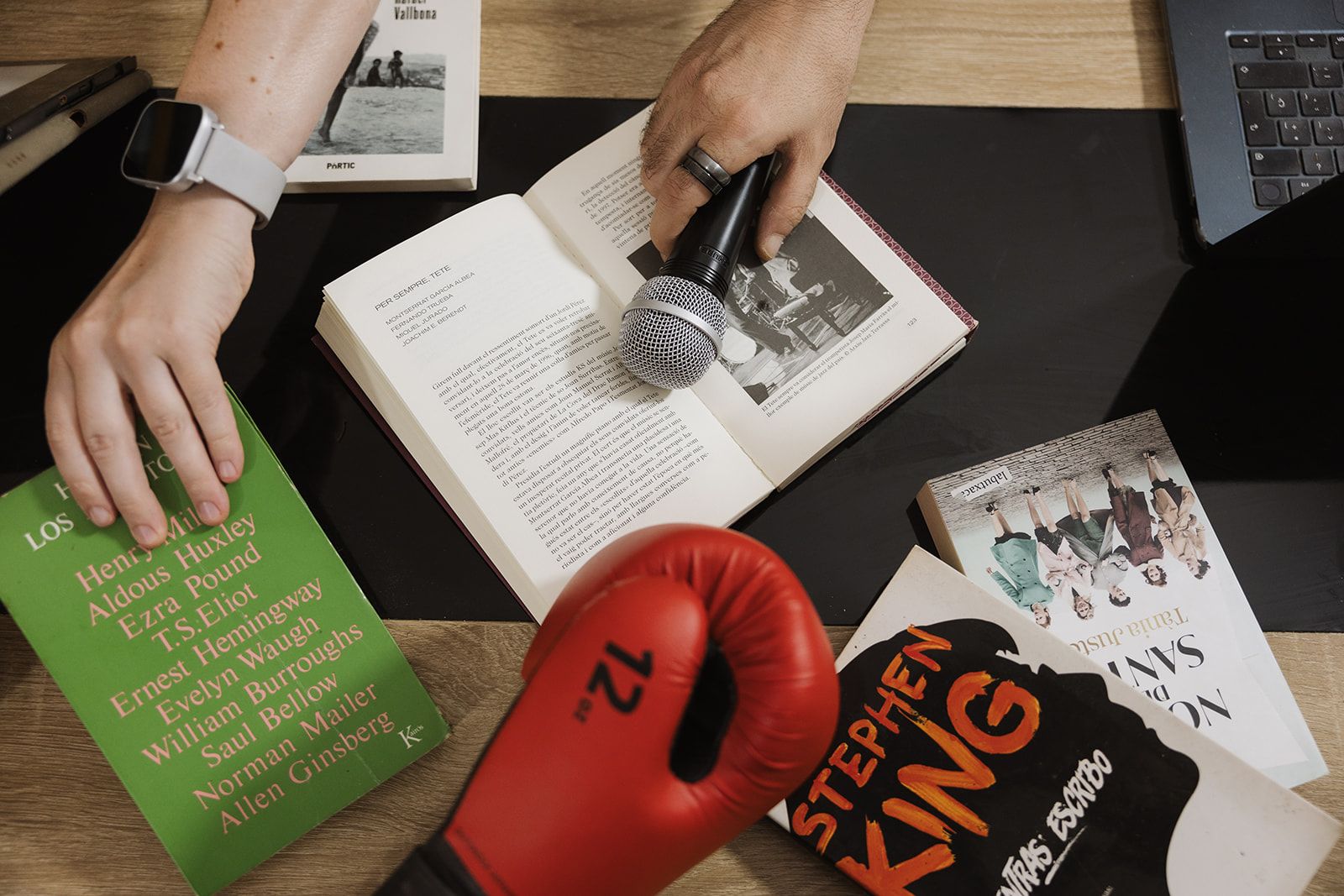 Un micrófono sobre un libro abierto, rodeado de libros y un guante de boxeo rojo